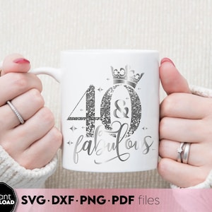 Puede incluir: Taza de cerámica blanca con un diseño de purpurina plateada que dice "40 & fabulous". Una corona está por encima del número 40. La taza está siendo sostenida por una persona que lleva un suéter blanco.
