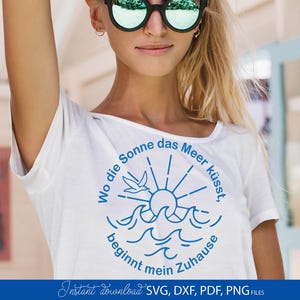 Pode incluir: Camiseta branca com um gráfico azul com um sol, ondas e um pássaro, com texto em alemão. O texto diz "Wo die Sonne das Meer küsst, beginnt mein Zuhause." A parte inferior da imagem tem o texto "Instant download SVG, DXF, PDF, PNG FILES."
