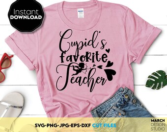 以下が含まれることがあります： 黒い文字で「Cupid's favorite teacher」と書かれたピンクのTシャツ。小さな黒いシルエットのキューピッドが矢を射っている。