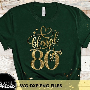 Op de afbeelding: Groen T-shirt met gouden glittertekst die "gezegend door God voor 80 jaar" luidt.