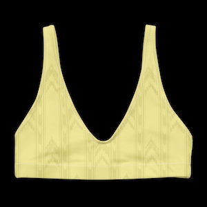 May include: A pale yellow sports bra featuring a deep V-neckline and wide shoulder straps. The garment is decorated with a subtle, repeating vertical pattern of chevron-like shapes and thin stripes in a slightly darker shade of yellow.
