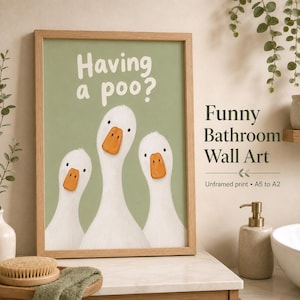 May include: A framed wall art print featuring three white geese with orange beaks against a sage green background. The text "Having a poo?" is printed in white at the top. The print is housed in a light-coloured wooden frame.