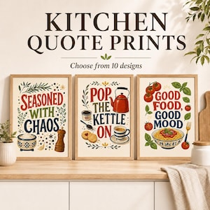 May include: Three rectangular wall art prints featuring kitchen-themed illustrations and text. The left print reads 'SEASONED WITH CHAOS', the centre 'POP THE KETTLE ON', and the right 'GOOD FOOD, GOOD MOOD', all displayed in wooden frames.