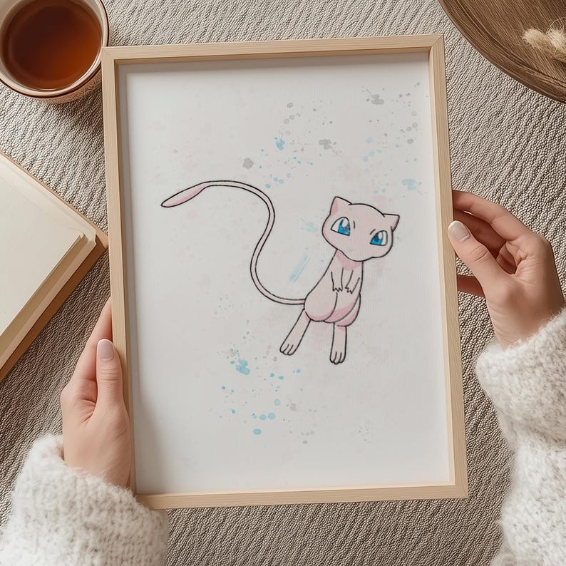 Close-up of hands holding framed Mew illustration – Someone holding a wooden-framed print of Mew from Pokémon over a table.