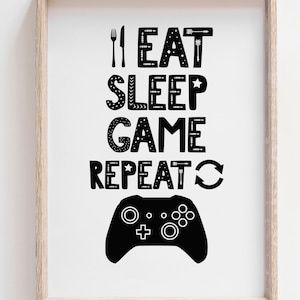 Puede incluir: Una l&aacute;mina enmarcada con el texto negro I EAT SLEEP GAME REPEAT, junto a un icono de tenedor y cuchillo, una estrella y un s&iacute;mbolo de flecha circular. Debajo del texto aparece la silueta negra de un mando de videojuegos sobre fondo blanco.