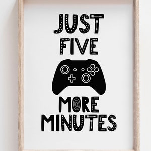 Puede incluir: Una l&aacute;mina enmarcada con el texto negro JUST FIVE MORE MINUTES y un gr&aacute;fico de un mando de videojuego negro en el centro. Las letras tienen varios patrones, incluyendo estrellas, flechas y l&iacute;neas sobre un fondo blanco en un marco de madera clara.