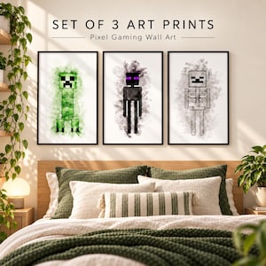 May include: A set of three art prints featuring pixelated gaming characters in black frames. The prints display a green creeper, a black enderman with purple eyes, and a white skeleton, each set against a watercolour-style background with text above.