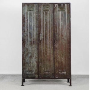 May include: A vintage metal locker with three doors. The locker is painted in a dark green color with rust and wear. The doors have a vertical ribbed design and are closed.