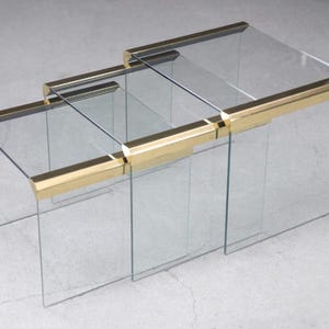 May include: A set of three glass nesting tables with gold metal trim. The tables are clear glass and have a modern design.