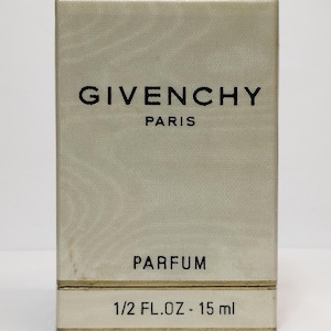 Op de afbeelding: Een rechthoekige parfumdoos met een getextureerd, lichtbeige oppervlak. De merknaam "GIVENCHY" is in het zwart gedrukt, boven "PARIS". Hieronder staat het woord "PARFUM" gedrukt. De onderste sectie luidt "1/2 FL.OZ - 15 ml".