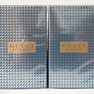 Könnte beinhalten: Zwei Schachteln Gucci Pour Homme II Duschgel. Die Verpackung hat ein geometrisches Muster in Grau- und Blautönen. Das Gucci-Logo ist in Gold auf einem rechteckigen Etikett. Jede Schachtel enthält 200 ml.