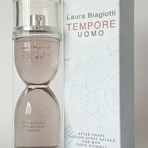 Pode incluir: Um frasco de vidro transparente em forma de ampulheta contendo um líquido claro, rotulado Laura Biagiotti TEMPORE UOMO AFTER SHAVE LOTION APRES RASAGE. Ao lado, uma caixa retangular com o mesmo texto e a inscrição 100 ml 3.4 fl oz.