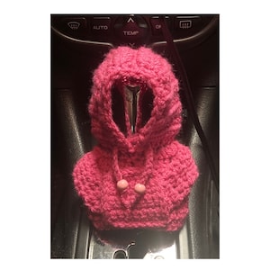 Könnte beinhalten: Ein rosa gehäkelter Automatik-Schalthebelbezug mit Kapuze und zwei rosa Knöpfen.