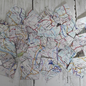 May include: A pile of torn pieces of paper maps, scattered on a white wooden surface. The maps are in various shades of blue, green, red, and yellow, with black lines and text.