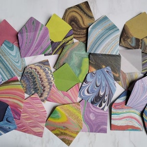 May include: A collection of colourful marbled paper envelopes. The envelopes are in various shades of blue, green, purple, pink, and yellow. Some of the envelopes have a metallic sheen.
