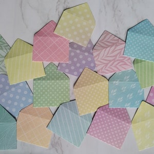 May include: A collection of pastel coloured envelopes with various patterns, including polka dots, stripes, and leaves.