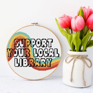 May include: A white embroidery hoop with a colorful rainbow design and the text "SUPPORT YOUR LOCAL LIBRARY" in black letters.