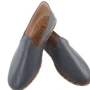 Peut inclure: Une paire de chaussures &agrave; enfiler en cuir gris avec une semelle et des coutures brunes. Les chaussures ont une &eacute;tiquette &agrave; l'int&eacute;rieur qui dit "Inshh" avec le mot "Genuine" au-dessus.