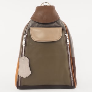 Könnte beinhalten: Ein mehrfarbiger Lederrucksack in Olivgrün, Beige, Braun und Orange. Die Tasche hat einen oberen Griff, eine Vordertasche und zwei Reißverschlussfächer. Ein kleines Etikett hängt an einem der Reißverschlüsse.