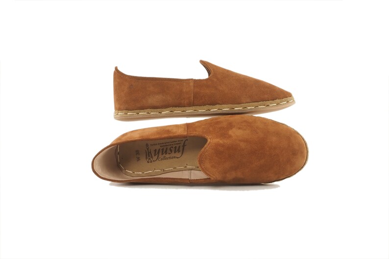 Pu&ograve; includere: Un paio di scarpe da uomo in pelle scamosciata marrone con un dettaglio di cucitura bianca attorno alla suola. Le scarpe sono realizzate da Yusuf Collection.