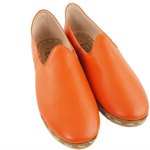May include: A pair of orange leather slip-on shoes with a textured finish and a white stitching detail around the sole.