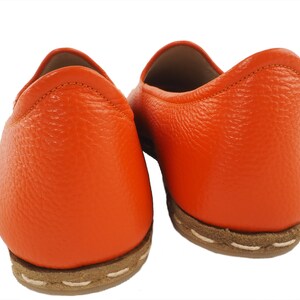 May include: A pair of orange leather slip-on shoes with a brown stitched sole.