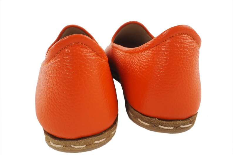 May include: A pair of orange leather slip-on shoes with a brown stitched sole.