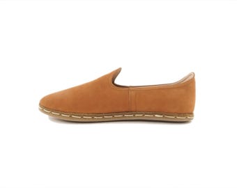 May include: A pair of brown leather slip-on shoes with a white stitching detail around the sole.