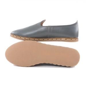 Peut inclure: Chaussures en cuir gris &agrave; enfiler avec une semelle en cuir marron et des coutures sur le bord.