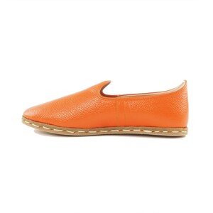 May include: A pair of orange leather slip-on shoes with a brown sole and white stitching.