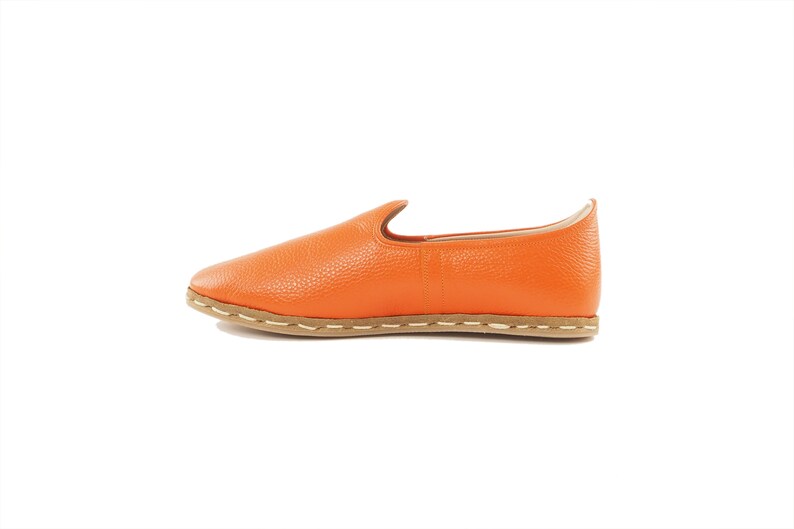 May include: A pair of orange leather slip-on shoes with a brown sole and white stitching.