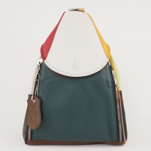 Puede incluir: Una mochila de cuero multicolor con una solapa blanca y una etiqueta de cuero marrón que dice "Prima". La mochila tiene un esquema de color verde, rojo, amarillo y marrón.