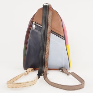 Può includere: Uno zaino in pelle multicolore con una tasca con cerniera e spalline regolabili. Lo zaino è realizzato con pannelli in pelle di diversi colori, tra cui blu scuro, marrone, verde, rosa e giallo.