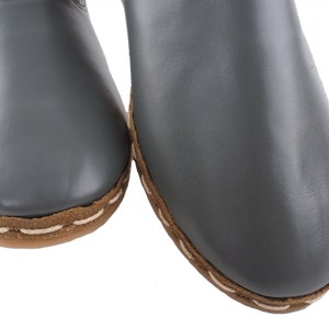 Peut inclure: Une paire de pantoufles en cuir gris avec des coutures brunes autour des bords.