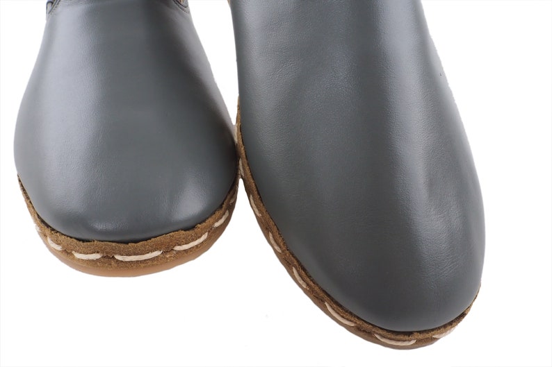 Peut inclure: Une paire de pantoufles en cuir gris avec des coutures brunes autour des bords.