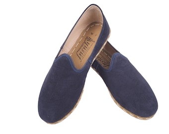 May include: A pair of dark blue suede slippers with a brown leather sole and the word "Insitu" printed on the inside.