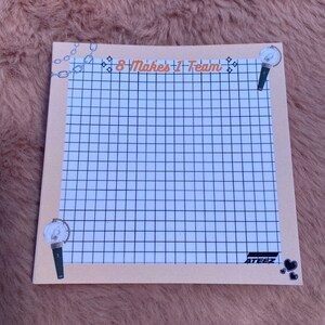 May include: A beige notepad with a grid pattern, featuring a black and white chain design at the top and the text "8 Makes 1 Team". The notepad also has a black and white light stick design on the right side and the text "ATEEZ" with black hearts at the bottom.