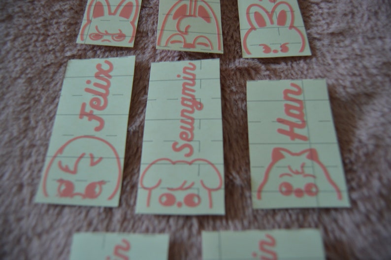 May include: Five pink and white stickers with different cartoon animal faces and names. The names are Felix, Seungmin, and Han.