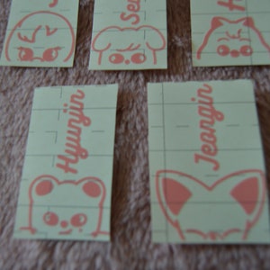 May include: Four pink and white stickers with cartoon animal faces and names. The names are "Hyunjin", "Jeongin", "Seungmin", and "Han".