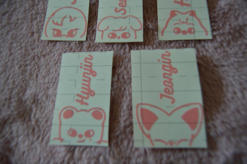 May include: Four pink and white stickers with cartoon animal faces and names. The names are "Hyunjin", "Jeongin", "Seungmin", and "Han".