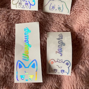 K&ouml;nnte beinhalten: Vier schimmernde holografische Aufkleber mit Comic-Tiergesichtern und Namen. Die Aufkleber zeigen einen Hund, eine Katze und zwei B&auml;ren. Die Namen auf den Aufklebern sind "Yu", "Yeon", "Wooyoung" und "Jeongho".