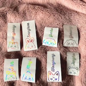K&ouml;nnte beinhalten: Acht schimmernde holografische Aufkleber mit verschiedenen Tierillustrationen und Namen. Die Namen sind: 'Seonghwa', 'Yunho', 'Yeosang', 'Hongjoong', 'San', 'Mingi', 'Wooyoung' und 'Jongho'.