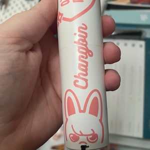May include: A white and pink handheld fan with a pink heart and the text "Charming" in Korean. The fan also features a pink bunny with a grumpy expression.