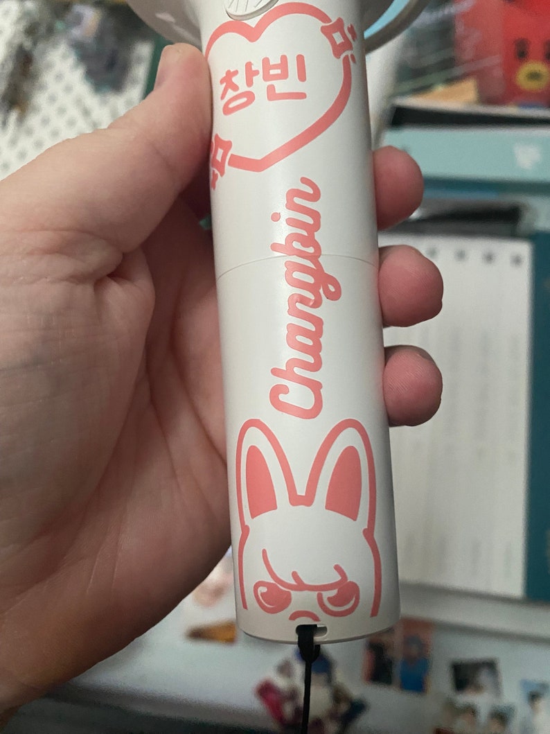 May include: A white and pink handheld fan with a pink heart and the text "Charming" in Korean. The fan also features a pink bunny with a grumpy expression.