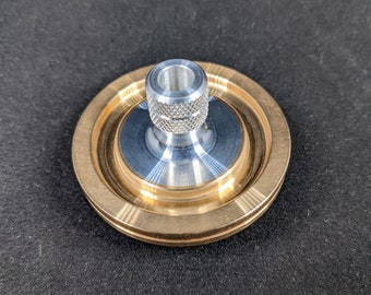 May include: A gold-colored metal spinning top with a silver metal center piece. The top has a ridged edge and a smooth, polished surface.