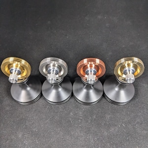 May include: Four spinning tops with different colored metal tops. The tops are silver, gold, copper, and brass. Each top has a black base.