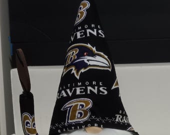 May include: A decorative gnome with a white beard and a black hat featuring the Baltimore Ravens logo. The gnome holds a brown staff and has black shoes with the team logo. The hat has the words "Baltimore Ravens" on it.