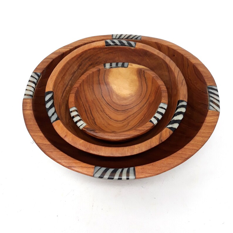 May include: A set of four wooden bowls in different sizes, nested together. The bowls are a warm brown with a natural wood grain. Each bowl features decorative zebra-striped accents around the rim.