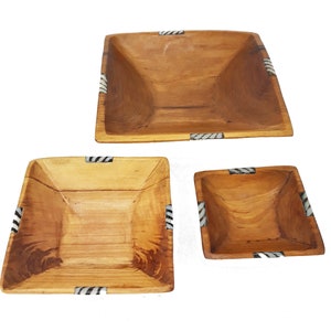 May include: A set of three wooden square bowls with a natural wood grain finish. Each bowl features black and white striped corner accents. The bowls are nested, in varying sizes, suitable for serving or display.