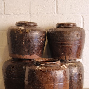 May include: A collection of five antique brown glazed ceramic jars. The jars have a rounded shape with a wide base and a narrower opening at the top. The jars are stacked on top of each other.